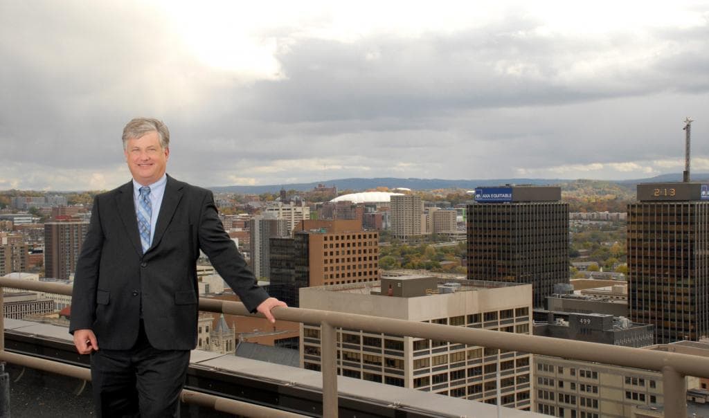 Bousquet Holstein attorney. Tom Taylor, seen in front of the Syracuse New York skyline. Tom is a real estate attorney in Syracuse.