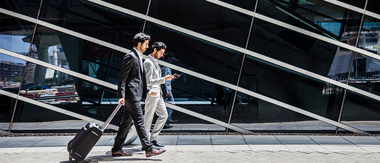 A photo of two businessmen in suits dragging a suitcase behind them introduces Bousquet Holstein's Employment immigration practice.